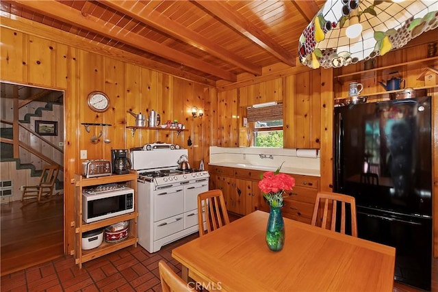 kitchen with white range with gas stovetop, black fridge, wooden walls, beam ceiling, and wood ceiling