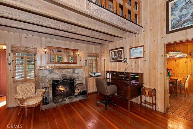 office with beam ceiling, a stone fireplace, wood walls, and hardwood / wood-style flooring