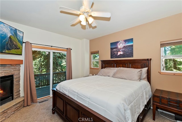 carpeted bedroom featuring ceiling fan, a stone fireplace, access to outside, and multiple windows