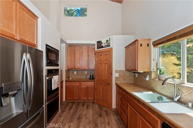 kitchen featuring tasteful backsplash, sink, black appliances, dark hardwood / wood-style flooring, and a high ceiling