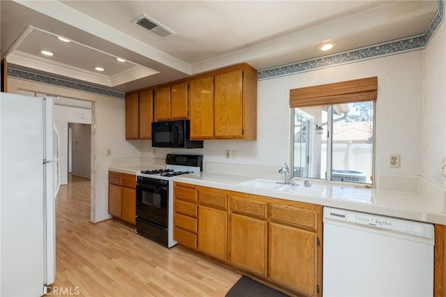 kitchen with sink, white appliances, light hardwood / wood-style flooring, a tray ceiling, and ornamental molding