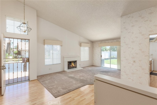 living room featuring high vaulted ceiling, hardwood / wood-style floors, a brick fireplace, and a textured ceiling