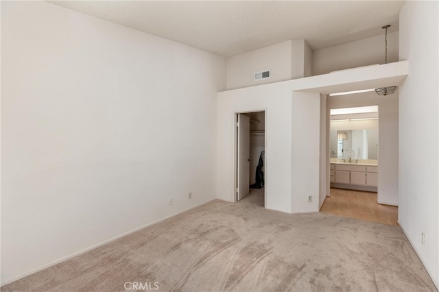 unfurnished bedroom featuring sink, connected bathroom, light carpet, a walk in closet, and a closet