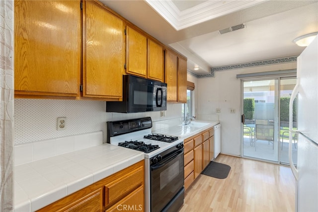 kitchen with tile countertops, sink, ornamental molding, white appliances, and light hardwood / wood-style flooring