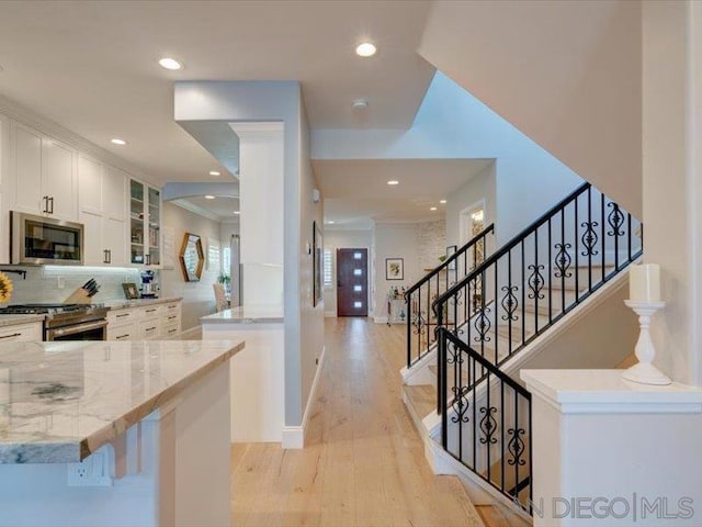 kitchen featuring kitchen peninsula, appliances with stainless steel finishes, light wood-type flooring, white cabinets, and light stone counters