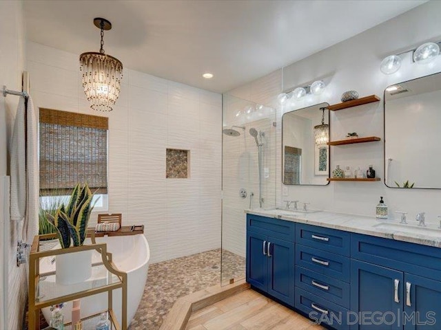 bathroom featuring hardwood / wood-style floors, vanity, an inviting chandelier, tile walls, and a tile shower