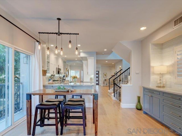 kitchen featuring white cabinetry, decorative backsplash, light hardwood / wood-style floors, hanging light fixtures, and gray cabinets