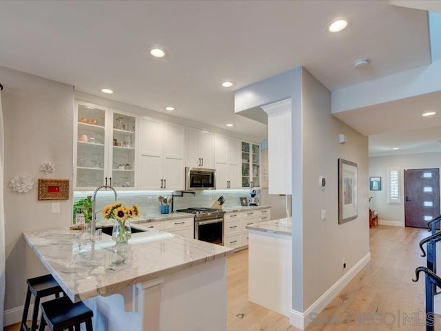 kitchen with white cabinetry, stainless steel appliances, kitchen peninsula, light stone counters, and a breakfast bar area