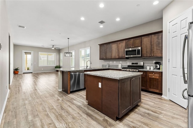 kitchen featuring decorative light fixtures, stainless steel appliances, a kitchen island, a sink, and dark brown cabinets