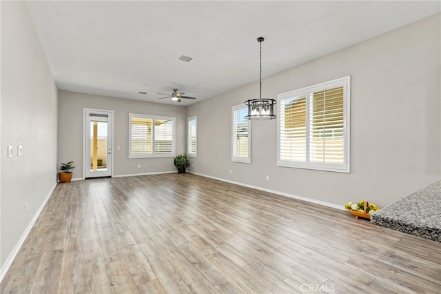 interior space featuring ceiling fan with notable chandelier, baseboards, light wood finished floors, and visible vents