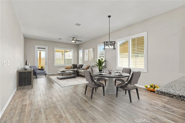dining room featuring light wood-style flooring, ceiling fan with notable chandelier, and baseboards