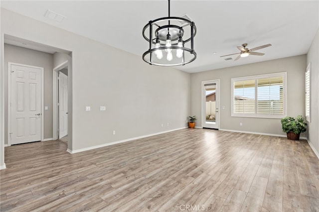 empty room with ceiling fan with notable chandelier, baseboards, light wood finished floors, and visible vents