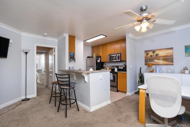 kitchen featuring light carpet, a kitchen bar, ceiling fan, appliances with stainless steel finishes, and ornamental molding