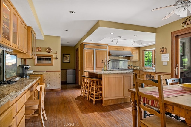 kitchen with light stone counters, a kitchen island, a kitchen bar, ceiling fan, and hardwood / wood-style floors