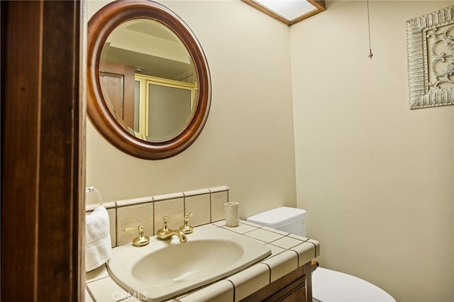 bathroom featuring a shower with shower door, vanity, and toilet