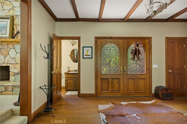 foyer with light wood-type flooring, beamed ceiling, and a stone fireplace