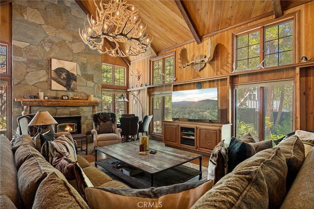 living room with a stone fireplace, an inviting chandelier, wood walls, and high vaulted ceiling