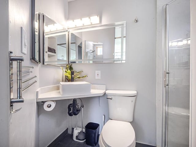 bathroom featuring sink, a shower with shower door, and toilet