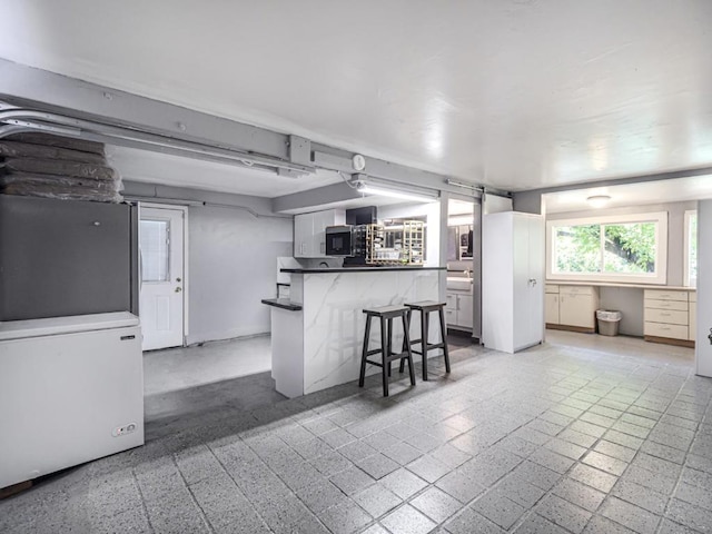 kitchen featuring white cabinetry, fridge, a kitchen breakfast bar, and kitchen peninsula