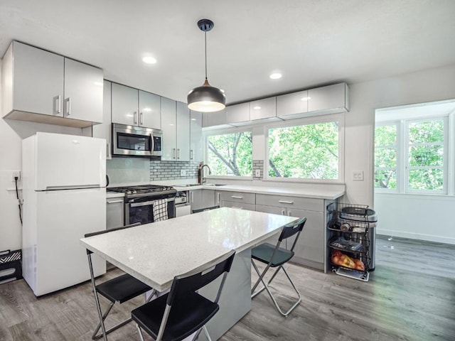 kitchen with pendant lighting, sink, light hardwood / wood-style flooring, stainless steel appliances, and tasteful backsplash