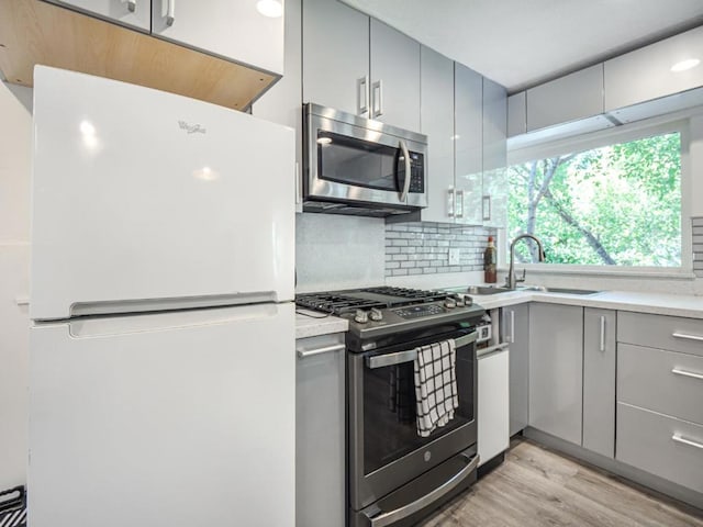 kitchen featuring sink, light wood-type flooring, appliances with stainless steel finishes, gray cabinets, and backsplash