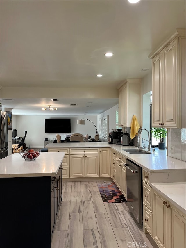 kitchen with sink, kitchen peninsula, light hardwood / wood-style flooring, cream cabinetry, and appliances with stainless steel finishes