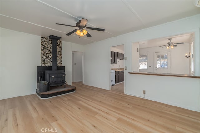 unfurnished living room with light hardwood / wood-style floors, ceiling fan, and a wood stove