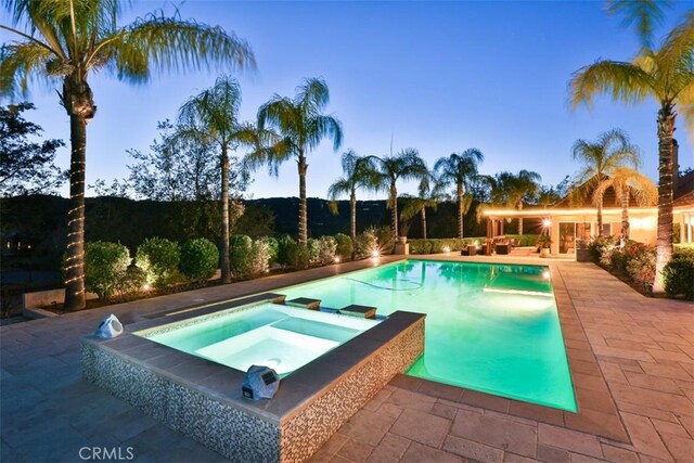 pool at dusk with a patio area and an in ground hot tub