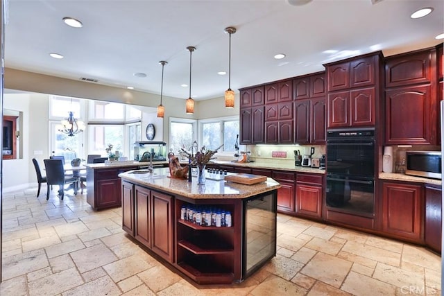 kitchen with pendant lighting, a center island with sink, black double oven, light stone countertops, and a chandelier