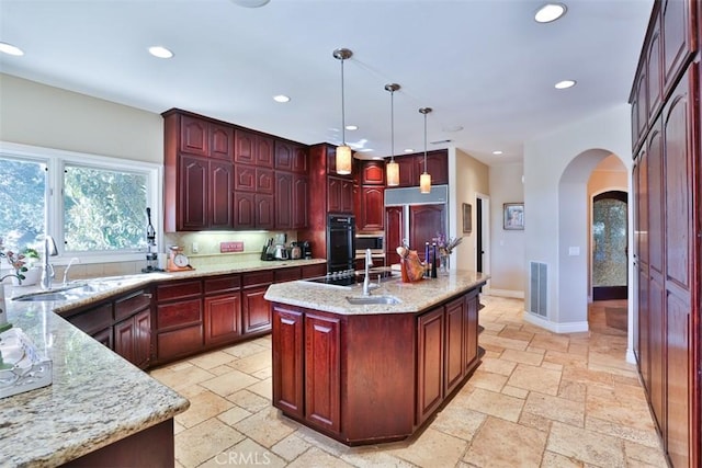 kitchen with light stone countertops, a center island with sink, pendant lighting, and paneled fridge