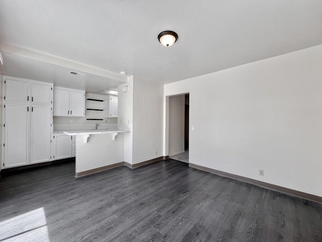 kitchen with white cabinetry, dark hardwood / wood-style flooring, sink, kitchen peninsula, and a breakfast bar area