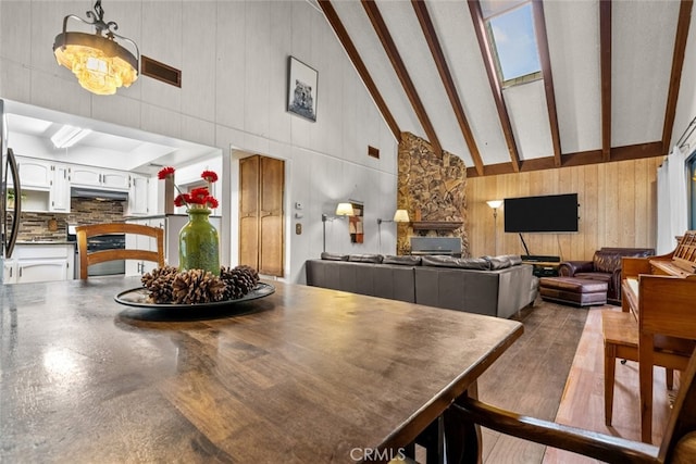 dining room featuring an inviting chandelier, wooden walls, high vaulted ceiling, and beamed ceiling