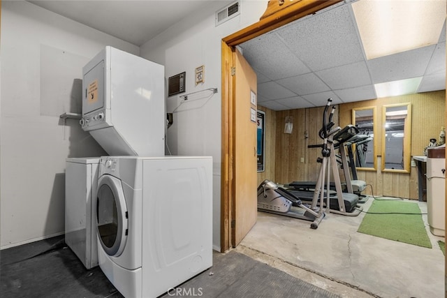 washroom featuring visible vents, wood walls, and stacked washing maching and dryer