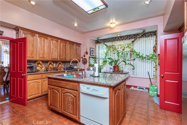 kitchen with a wealth of natural light, dishwasher, a kitchen island with sink, sink, and backsplash