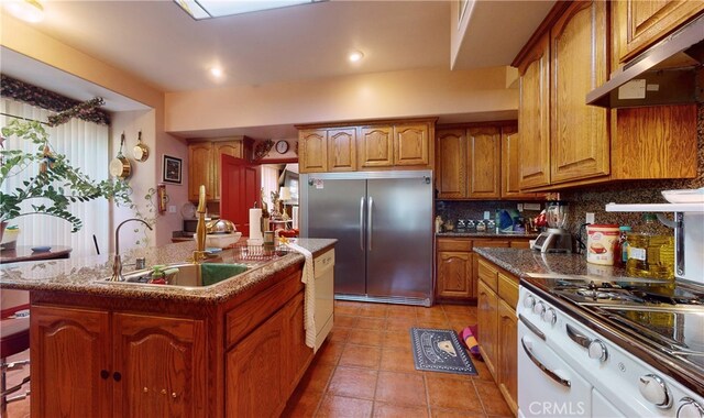 kitchen featuring tasteful backsplash, sink, range hood, white appliances, and a center island with sink