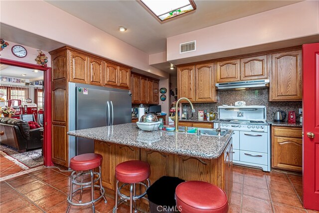 kitchen featuring a kitchen breakfast bar, white range oven, an island with sink, backsplash, and sink