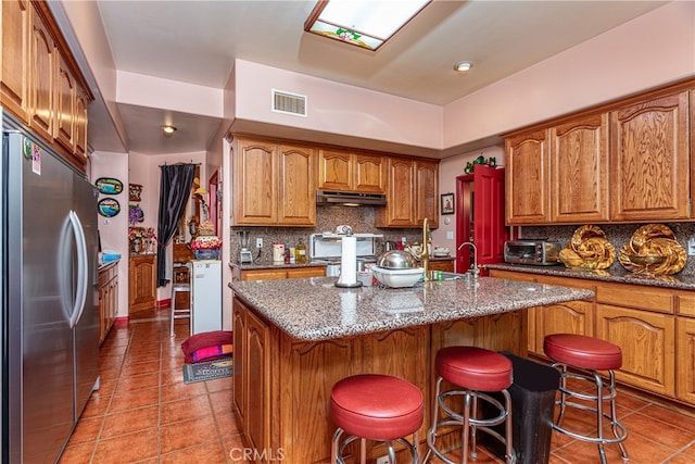 kitchen with a kitchen island with sink, a breakfast bar area, stone counters, decorative backsplash, and stainless steel appliances