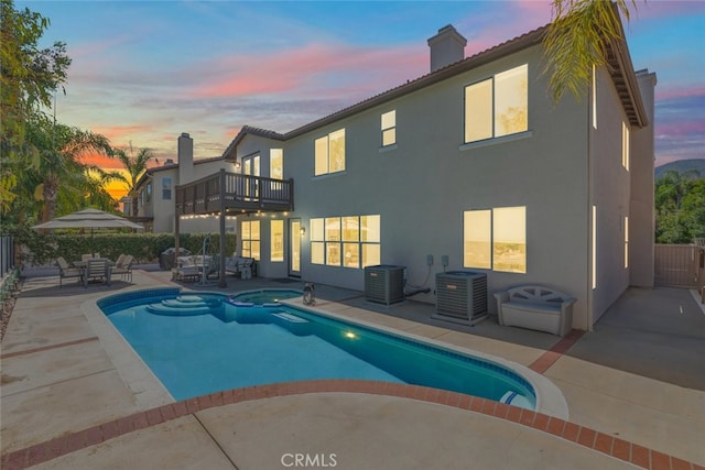 pool at dusk with a patio, an in ground hot tub, and central AC unit