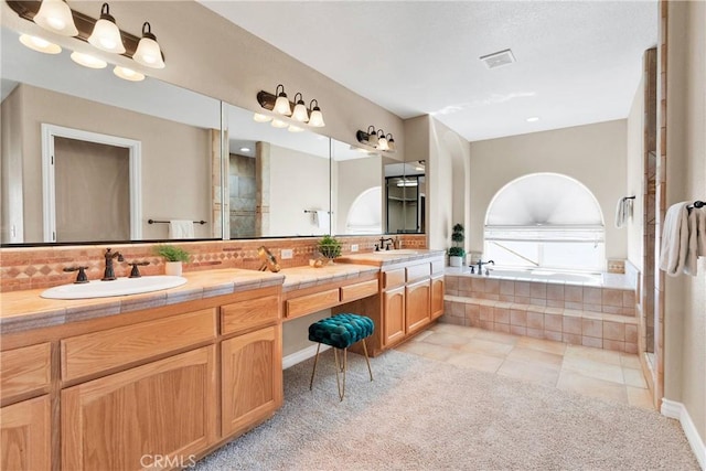 bathroom with tasteful backsplash, vanity, tile patterned flooring, and a relaxing tiled tub