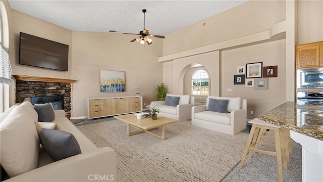 living room with a textured ceiling, ceiling fan, and a stone fireplace