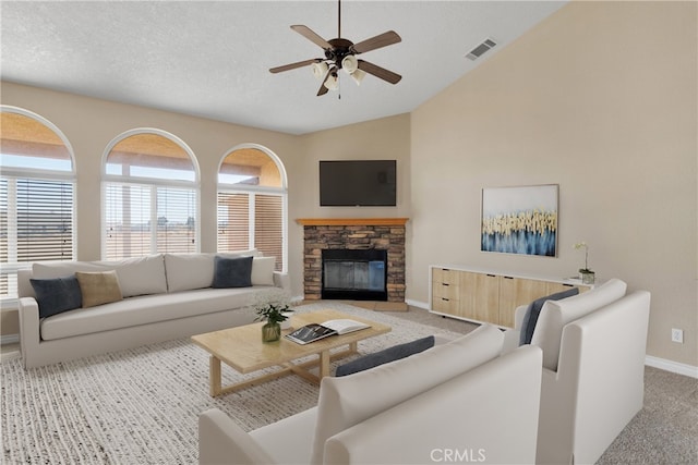 carpeted living room featuring ceiling fan, a textured ceiling, a stone fireplace, and vaulted ceiling