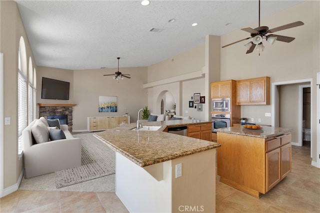 kitchen featuring a large island with sink, stainless steel appliances, a fireplace, sink, and ceiling fan