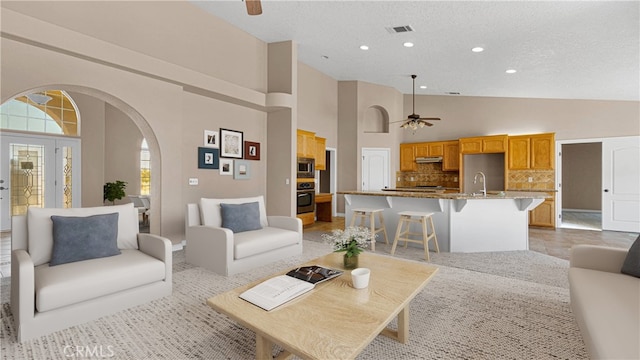 living room featuring a textured ceiling, ceiling fan, high vaulted ceiling, and sink