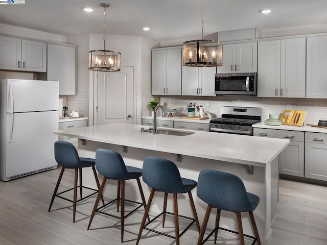 kitchen featuring decorative light fixtures, a center island with sink, stainless steel appliances, and sink