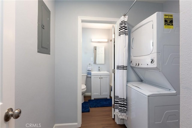 clothes washing area with stacked washer / dryer, wood-type flooring, sink, and electric panel