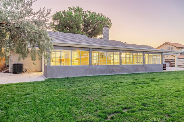 back house at dusk with a patio, a yard, and central air condition unit