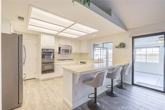 kitchen with a breakfast bar, light hardwood / wood-style floors, white cabinets, stainless steel appliances, and tile countertops