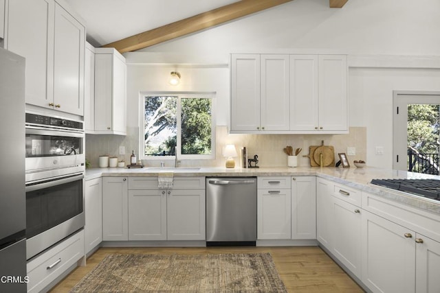 kitchen featuring backsplash, sink, vaulted ceiling with beams, appliances with stainless steel finishes, and white cabinetry