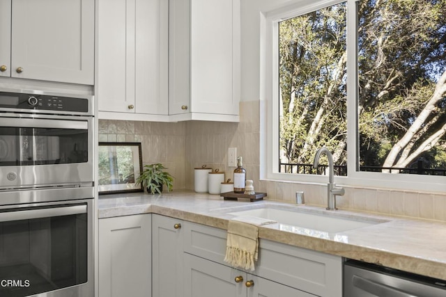 kitchen featuring white cabinetry, sink, stainless steel appliances, light stone counters, and decorative backsplash