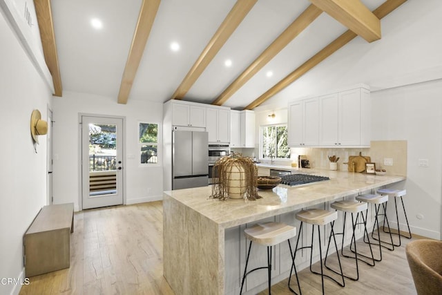 kitchen with white cabinets, vaulted ceiling with beams, appliances with stainless steel finishes, light hardwood / wood-style floors, and kitchen peninsula